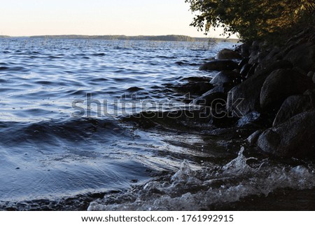 Waves washing the rocks of the lake shoreline in the shade. Close up. The nature of Scandinavia in summer