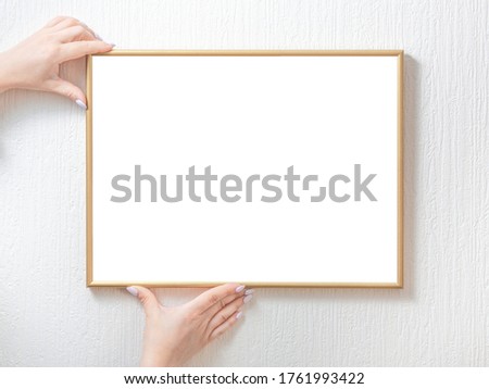 Woman hands holding white empty photo frame hanging on wall. Picture frame mockup
