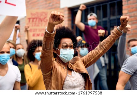 Black woman with raised fists wearing protective face mask while supporting anti-racism demonstrations.  Royalty-Free Stock Photo #1761997538