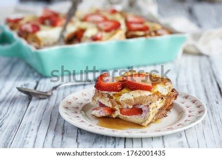 Strawberry cheesecake French toast casserole with maple syrup. Made with cream cheese and strawberries. Selective focus with blurred background.