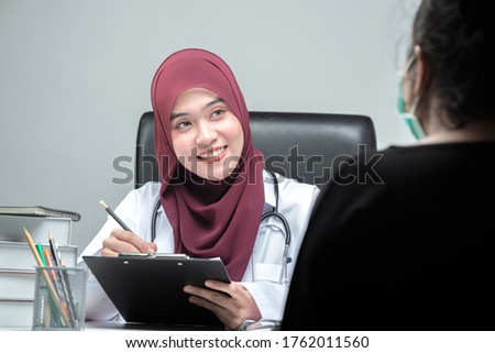 The Asian Muslim woman doctor was sitting at the patient's examination table and was examining and talking about the patient with a smiling and worried face.
