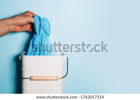 Hand in medical gloves throws medical mask into trash can on blue background. Quarantine over. Covid 19. Concept of coronavirus end. Banner with copy space. Stay safe. Health protection equipment.
