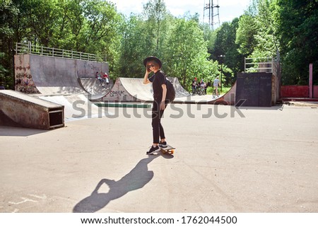 Pretty smiling teenage girl in hat and sunglasses rides skateboard in skatepark, active and sport lifestyle