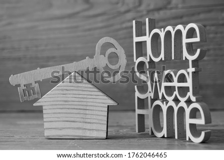 Key and wooden house with text plate - home sweet home - on wooden background. stay home idea.