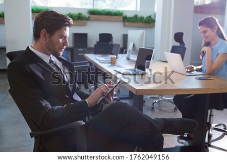 Businessman using digital tablet while female executive using laptop in office