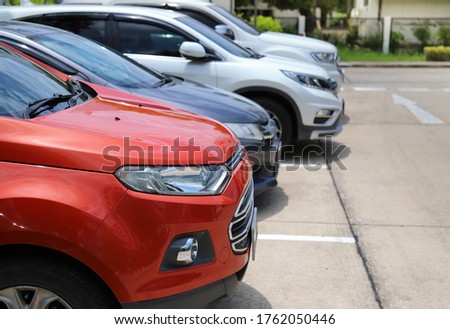 Closeup of front side of red car with other cars parking in outdoor parking area  in bright sunny day.