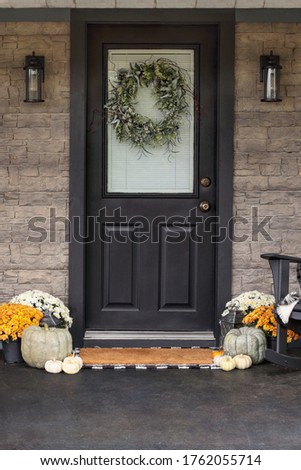 Front porch decorated for Thanksgiving Day with homemade wreath hanging on door. Heirloom gourds,  white pumpkins, and mums giving an inviting atmosphere.
