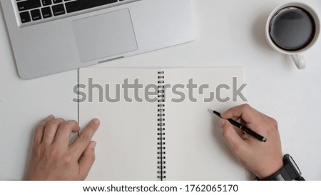 hands businessman writing on book and laptop on white table in office.