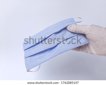 A hand with white latex glove, holding blue mask. Isolated in white background
