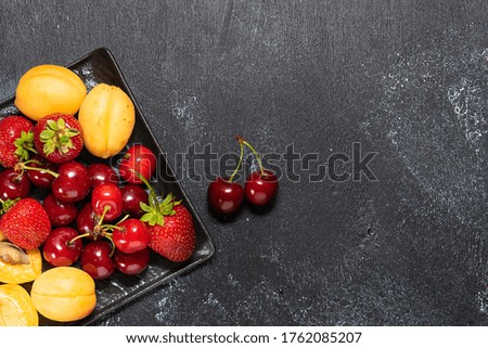Fresh summer fruit on black plate on dark rustic background top view. Healthy diet food concept.