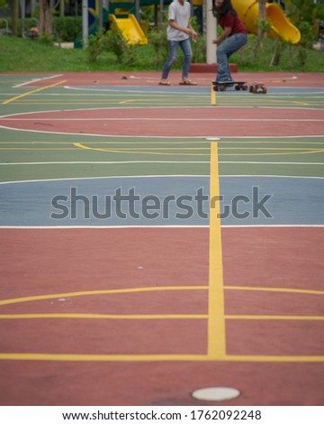 Basketball court with skateboarders in the background.