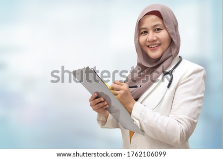 Asian muslim female doctor wearing hijab with stethoscope in white coat holding clipboard, ready to serve her medical patient, write medical record diagnosis