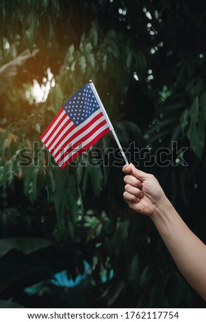 Woman hand holding USA Flag on green forest. 4th July American Independence Day
