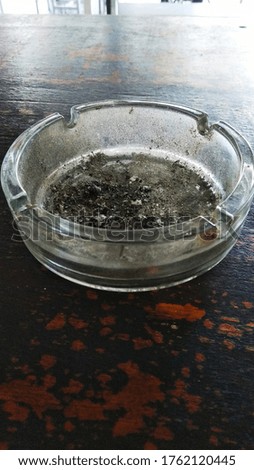 This picture shows an ashtray made of glass with the remaining cigarette ash in it
