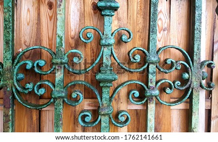 The texture of a metal strong fence, a wall with a beautiful pattern of wrought iron flower with castings and branches from curved rods. The background from wood.