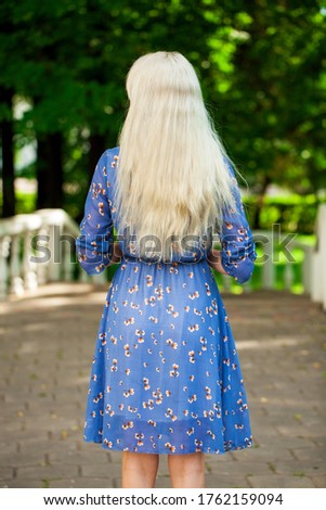 Portrait of a young beautiful blonde girl in blue flowers dress walking in summer park