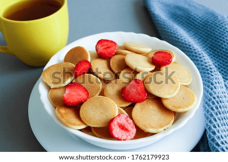 Bowl with tiny pancake cereal on a grey background. Mini cereal pancakes with strawberries. High quality photo
