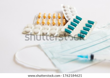 portion of pills on the background of a three-layer medical mask with rubber ear straps, a syringe and various medicines, tablets.The concept of medicine