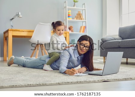 Multitasking for work at home moms. Young woman doing online job on laptop while her daughter sitting on her back