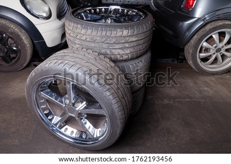 A set of expensive stylish winter tires for a German car with chrome wheels in the garage against the background of cars stored in the summer season, spare wheels. Royalty-Free Stock Photo #1762193456