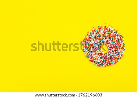 Multicolored sugar pastry topping in form of donut on yellow background. Funny food. Top view. Copy space