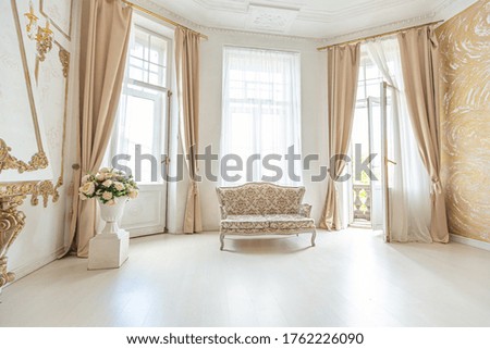 luxurious expensive interior of a large baroque royal living room. antique furniture, gold trim, huge windows, fireplace with gold stucco on the walls. full of daylight Royalty-Free Stock Photo #1762226090