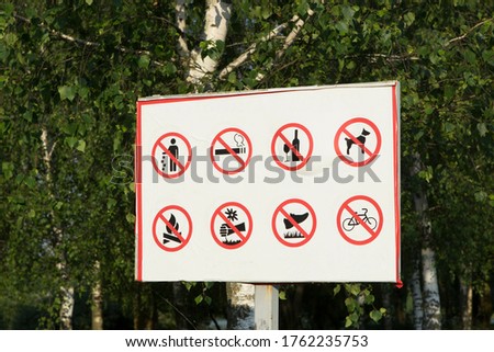 Many prohibition signs on one poster in a summer park. Do not litter, do not smoke, do not drink alcohol, do not light fires.