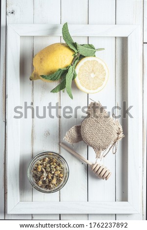 Chamomile infusion in a frame on white old wooden board with lemon and jar of honey