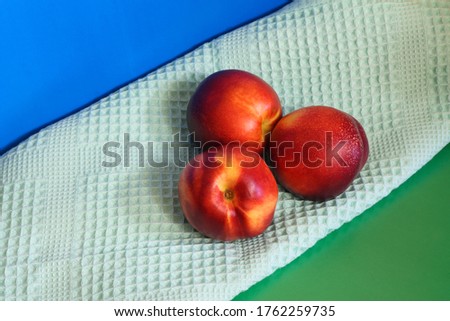 Three nectarines next to a towel on a green and blue background.