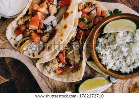 Close up of Mexican fiesta of food tacos and burritos with cheese, onions, chicken, pico de gallo, cilantro lime rice and sour cream