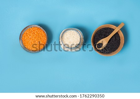 Variety of seeds of white and black sesame seeds of orange lentils in glass jars on a wooden plate a bamboo spoon, top view. Zero waste.