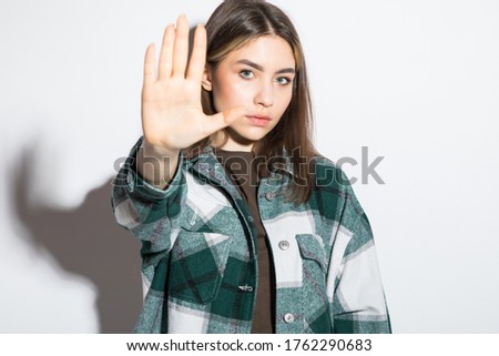 Portrait of an upset young girl in plaid shirt standing and showing stop gesture over white background