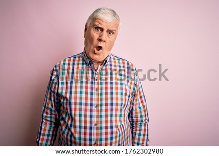 Senior handsome hoary man wearing casual colorful shirt over isolated pink background In shock face, looking skeptical and sarcastic, surprised with open mouth