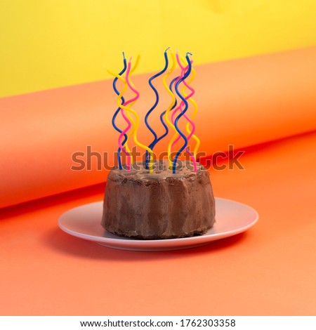 Homemade chocolate birthday cake with curves colorful candles on orange yellow background.