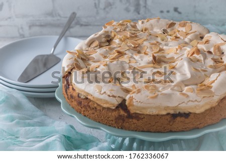Delicious homemade rhubarb cake on a mint green cake plate, topped with sweet meringue and roasted almonds and decorated with summer flower. Mint green cloth and white background.