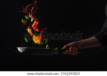 Cooking seafood, frying in a pan with vegetables, veggie healthy food, on a black background, menu and restaurant business