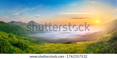Idyllic landscape with green grass covered morning mountains with distant peaks and wide valley full of thick white cloudy fog. Royalty-Free Stock Photo #1762357532