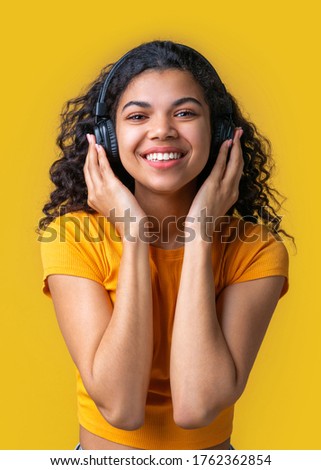 Vertical shot of cute dark skinned girl having fun listening to music with wireless headphones.