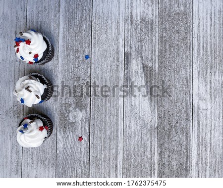 three white muffins, cupcakes with American-colored stars on a white rough wooden board are on the left background for text, free space for design, high quality photo for USA Independence Day