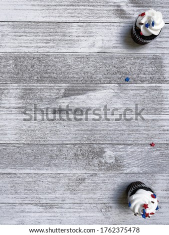 two white muffins, cupcakes with American-colored stars on a white rough wooden board are on the left, vertical background for text, free space for design, high quality photo for USA Independence Day