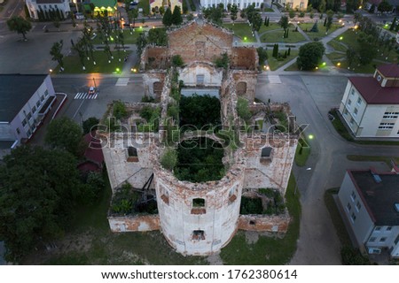 A beautiful crumbling church in the city center, overgrown with trees with a stork nest on top. Eastern Europe. Aerial photography