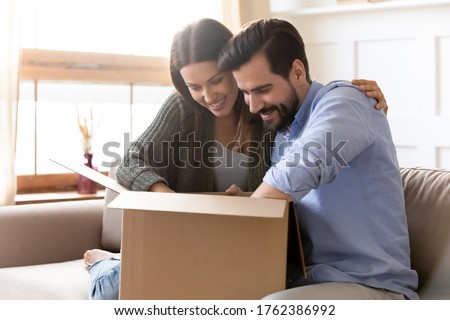 Curious young couple unpacking cardboard parcel package together, looking into open carton box, satisfied clients customers received online store order, good delivery service concept Royalty-Free Stock Photo #1762386992