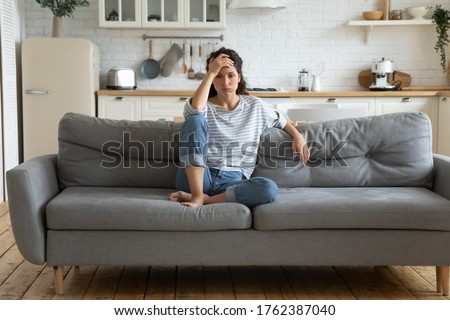 Tired upset woman worried about tiredness from domestic work sitting at couch. Frustrating mom stressful feels heaviness and headache at home. Fatigue parent trying relaxing in living room.