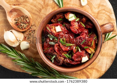 Sun-dried tomatoes with garlic, rosemary and spices in a clay bowl on an olive wood cutting board, top view, flat lay