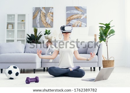 Young mom spending time with her little kids, meditating in lotus yoga position while her children playing at home on background.