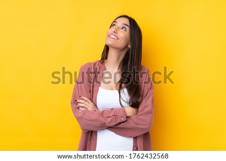 Young brunette woman over isolated yellow background looking up while smiling Royalty-Free Stock Photo #1762432568
