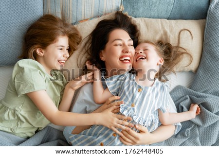 A nice girls and their mother enjoy sunny morning. Good time at home. Children waking up from sleep. Family playing on the bed in the bedroom.   