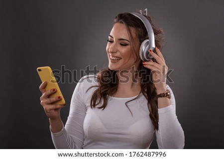 Woman with headphones on her head and mobile phone on hand listen music and enjoy studio shoot