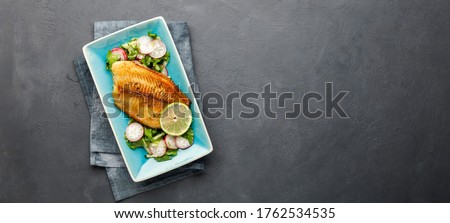 Grilled fish sea bass fillet with green lettuce and radish. Black stone background. Top view with copy space. Royalty-Free Stock Photo #1762534535