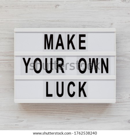 'Make your own luck' on a lightbox on a white wooden surface, top view. Flat lay, from above, overhead. Close-up.